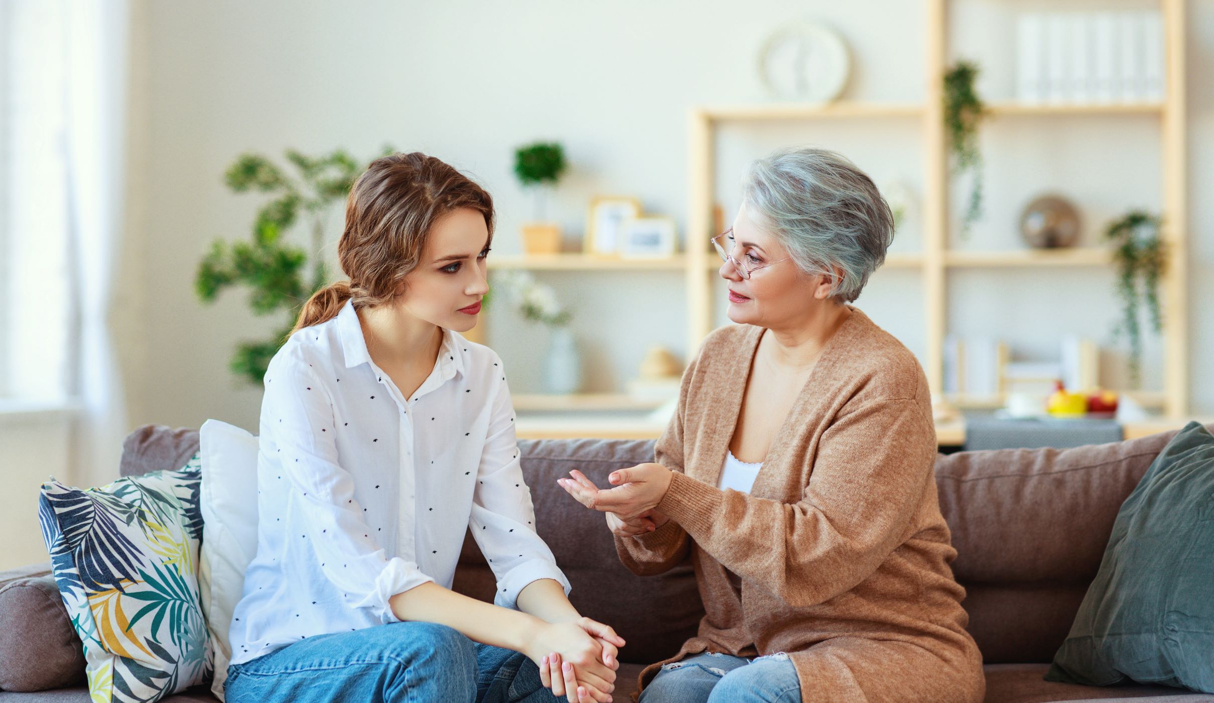 Senior mother sits on sofa with adult daughter having a tense conversation.